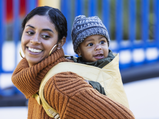 Mère qui porte son enfant dans un porte-bébé au dos Mère qui porte son enfant dans un porte-bébé au dos