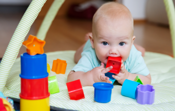 Un bébé couché sur le ventre joue avec des formes en plastique colorées.