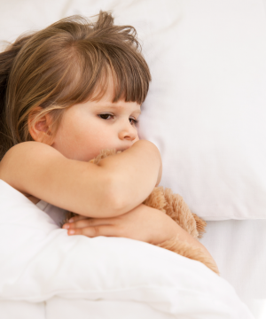 Fillette qui a peur dans son lit et qui serre un ourson en peluche dans ses bras.